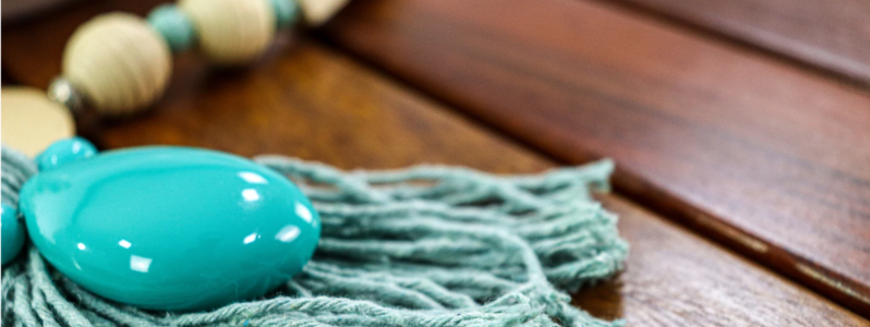 Colar de mesa decorativo com contas de madeira e pingente azul sobre mesa de madeira.