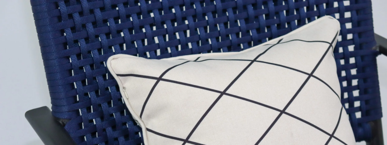Detalhe da poltrona tricô náutico em tom azul marinho, com trançado resistente e almofada decorativa geométrica em destaque.