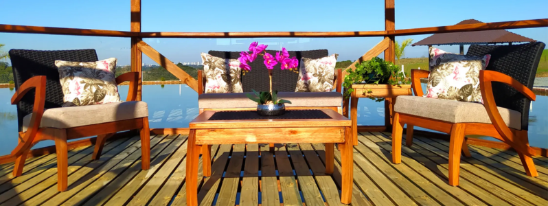 Conjunto de móveis de área externa com sofá que pode molhar em corda náutica, mesa de madeira e poltronas, decorado com almofadas florais, posicionado sobre deck com vista para lago ao ar livre