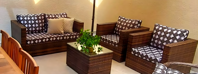 Conjunto de sofá beira de piscina em fibra sintética com almofadas estampadas, acompanhado de mesa central de vidro em área externa decorada.